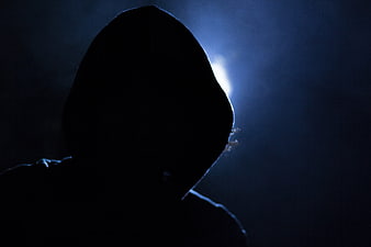 Silhouette of hooded figure in dark blue light