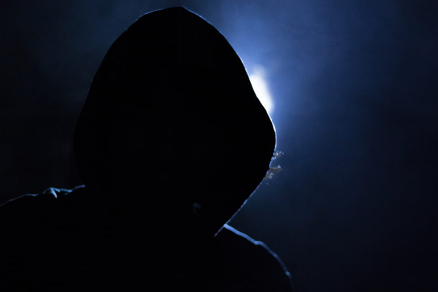 Silhouette of hooded figure in dark blue light