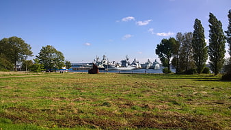 Naval ships docked in harbor with grassy park foreground