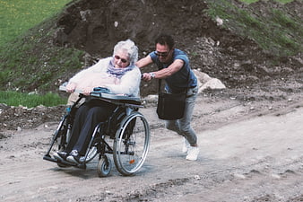 Man Pushing Elderly Woman In Wheelchair On Dirt Path