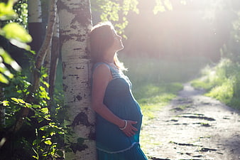 Pregnant woman leaning against birch tree in sunlight