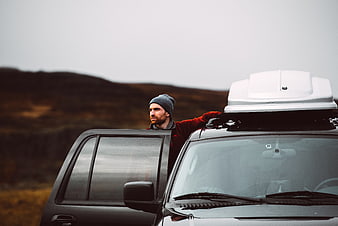 Man in beanie standing by SUV with roof box in highlands
