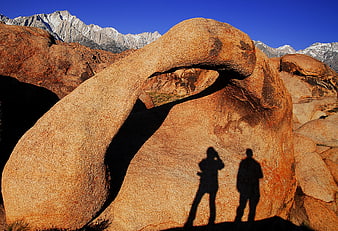 Silhouettes of Hikers Under Natural Rock Arch in Desert