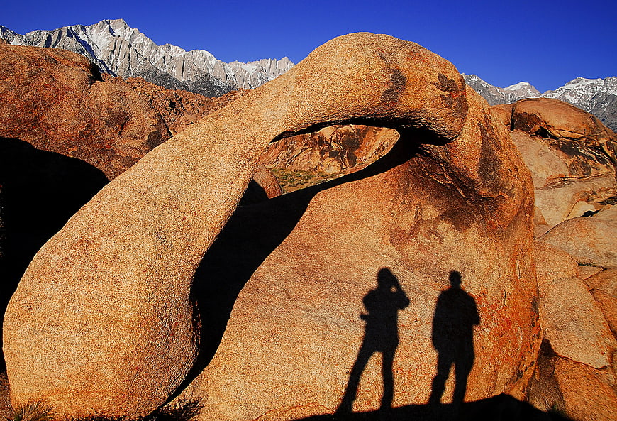 Silhouettes of Hikers Under Natural Rock Arch in Desert