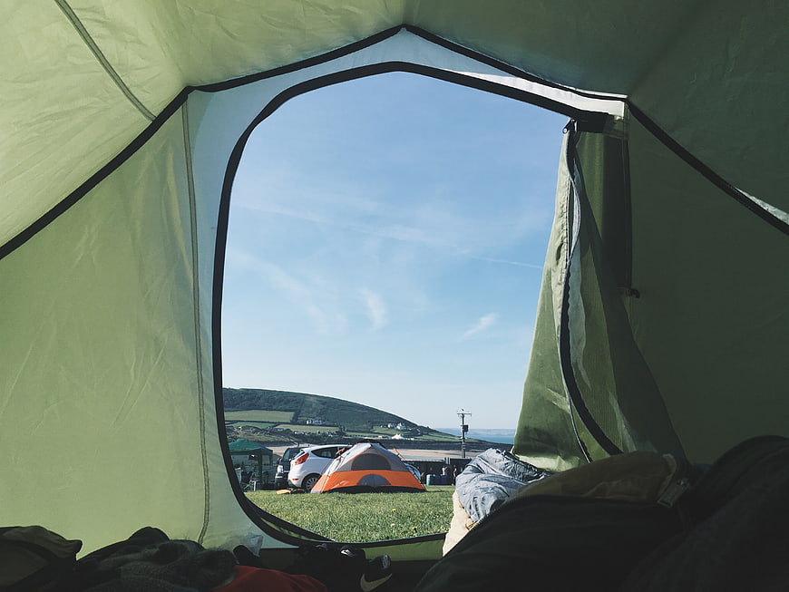 View from inside a green camping tent looking out at a sunny campsite