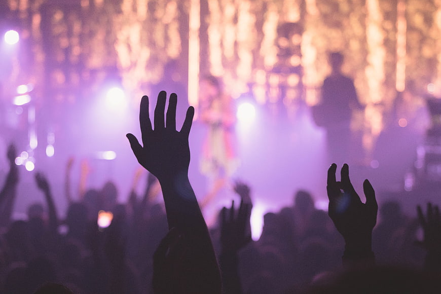 Silhouetted crowd hands raised at a vibrant concert