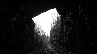 Black and white view of abandoned railway tracks exiting a dark tunnel