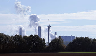Coal power plant smokestacks and wind turbine in rural landscape