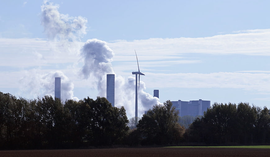 Coal power plant smokestacks and wind turbine in rural landscape