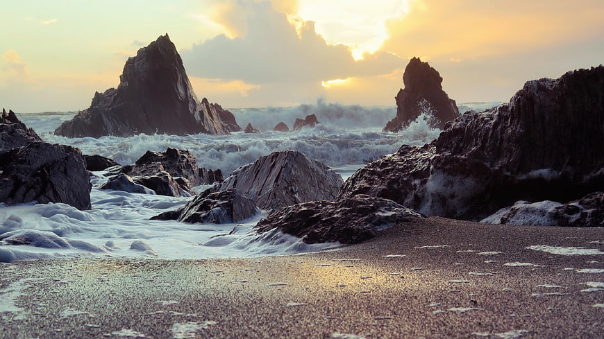 Dramatic Sunset Over Rocky Coastline with Crashing Waves