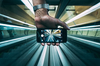 Hand holding smartphone capturing motion blur on escalator