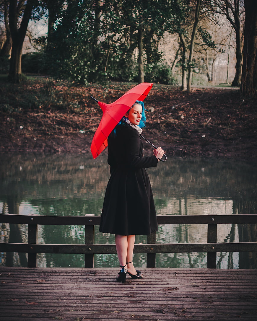 Woman with Blue Hair Holding Red Umbrella on Wooden Bridge