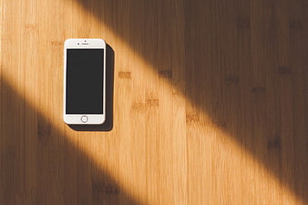 White Smartphone on Wooden Surface with Sunlight Shadows