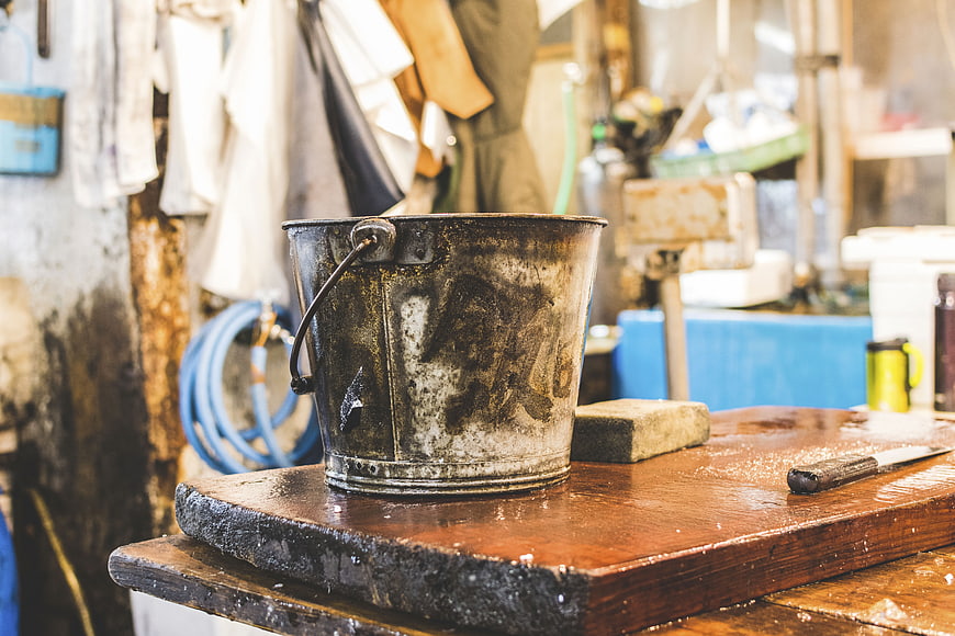 Weathered metal bucket on wet wooden workbench in workshop