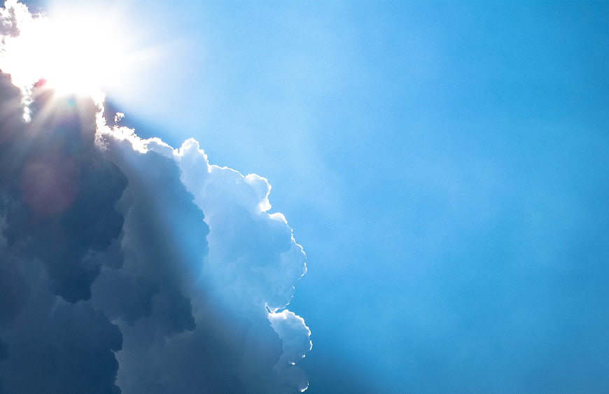 Sun rays breaking through clouds in blue sky
