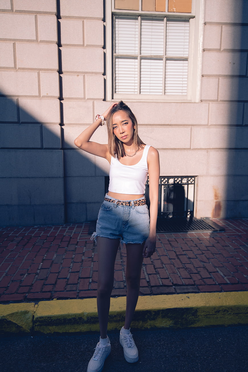 Young woman in white top and denim shorts posing on city street