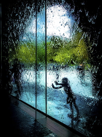 Silhouette of child playing behind wet glass wall