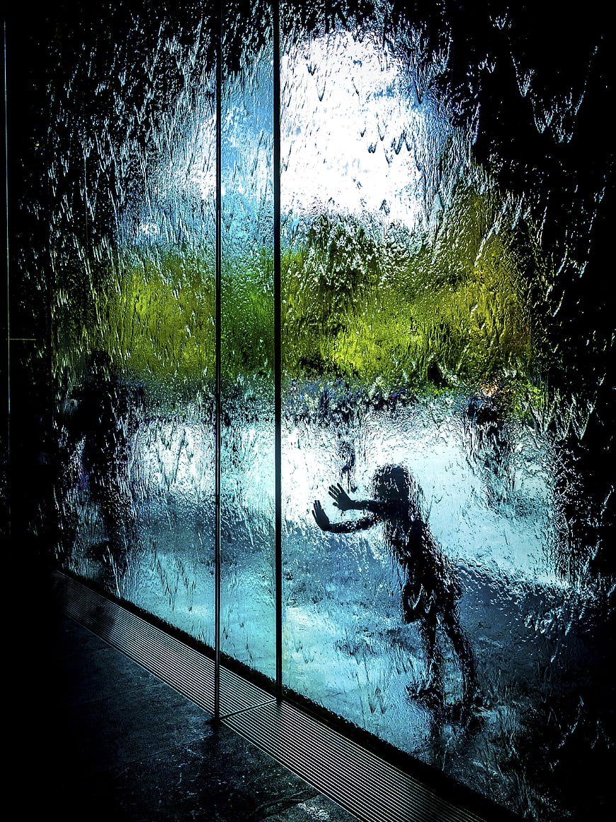 Silhouette of child playing behind wet glass wall