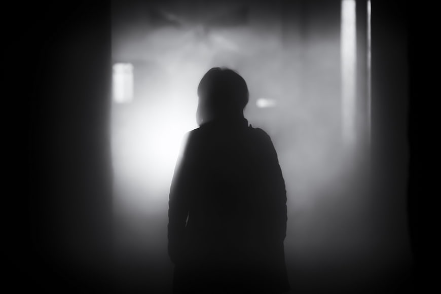 Silhouette of a person standing in dark foggy atmosphere