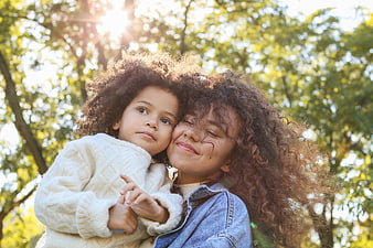 Mother and daughter hugging outdoors in sunlight