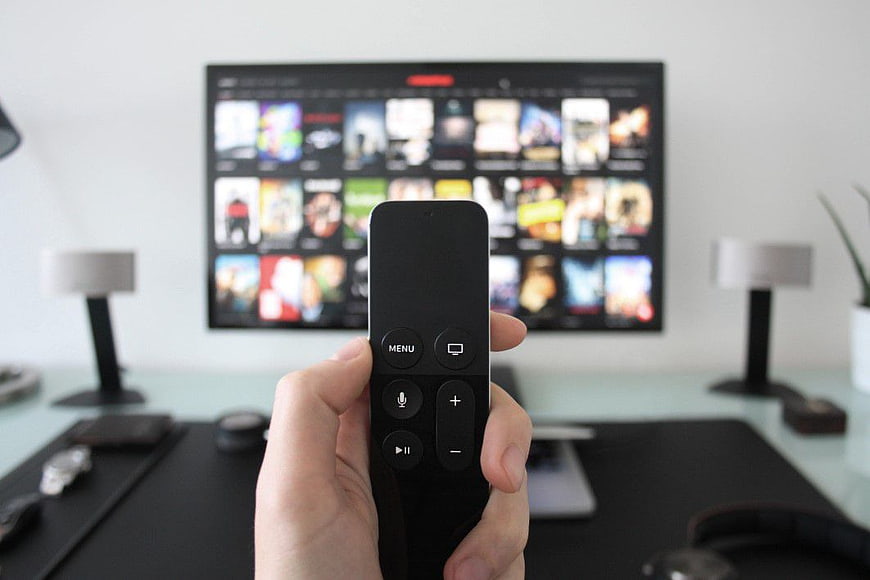 Hand holding Apple TV remote with streaming menu on TV