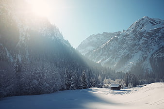 Serene Winter Mountain Landscape with Snowy Cabin and Sunlight