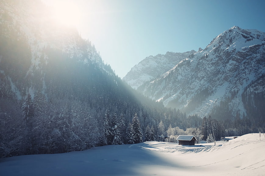 Serene Winter Mountain Landscape with Snowy Cabin and Sunlight