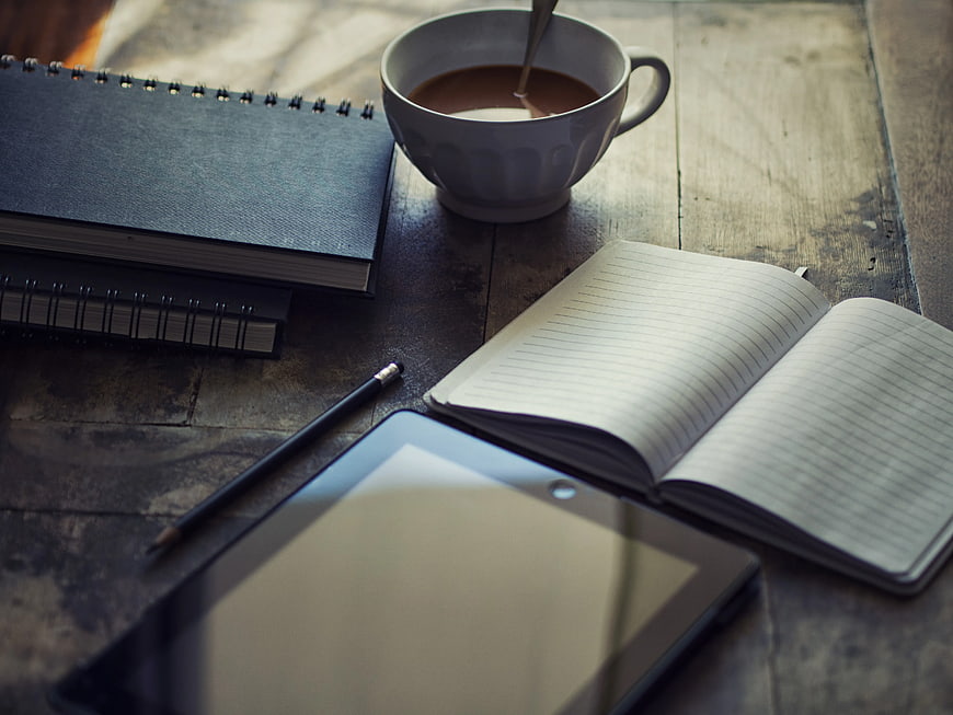 Workspace with coffee, notebook, and tablet on wooden table