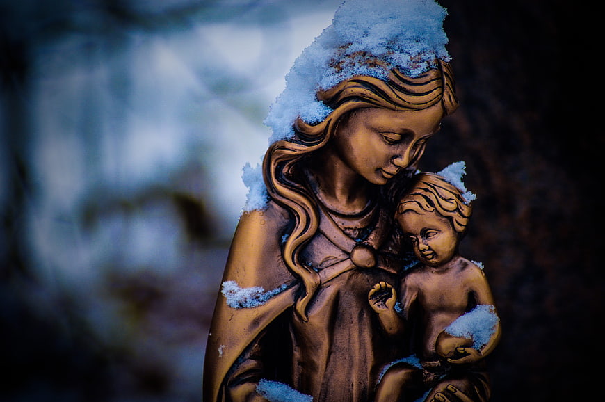 Snow-covered bronze statue of Mother Mary holding baby Jesus