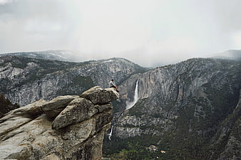 Man sitting on cliff edge overlooking waterfall and mountains