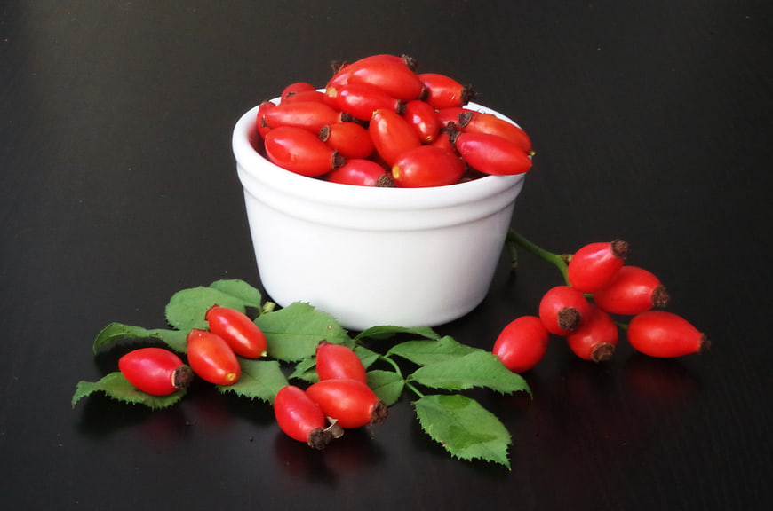 Fresh Rose Hips in White Bowl on Black Background