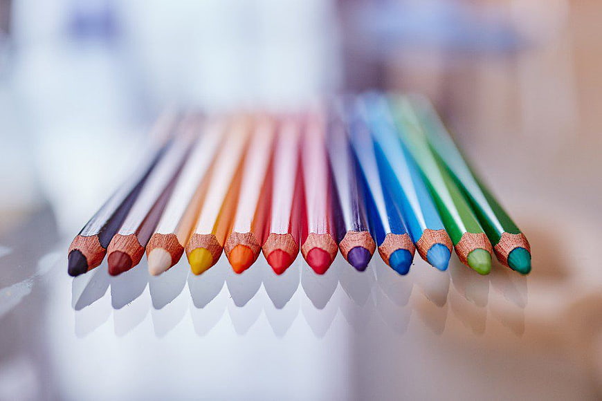 Row of colorful pencils on reflective surface