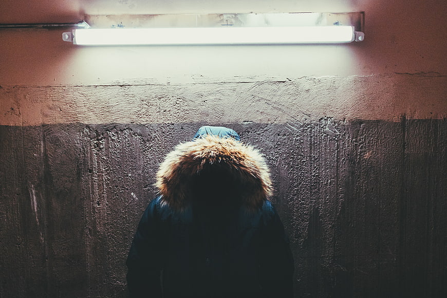 Anonymous figure in fur hood under fluorescent light