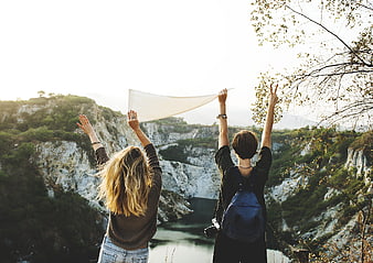 Two female friends hiking with arms raised overlooking canyon