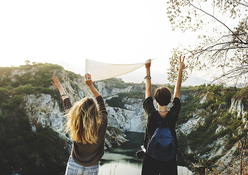 Two female friends hiking with arms raised overlooking canyon
