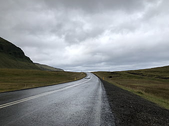 Wet asphalt road winding through green hills under cloudy sky