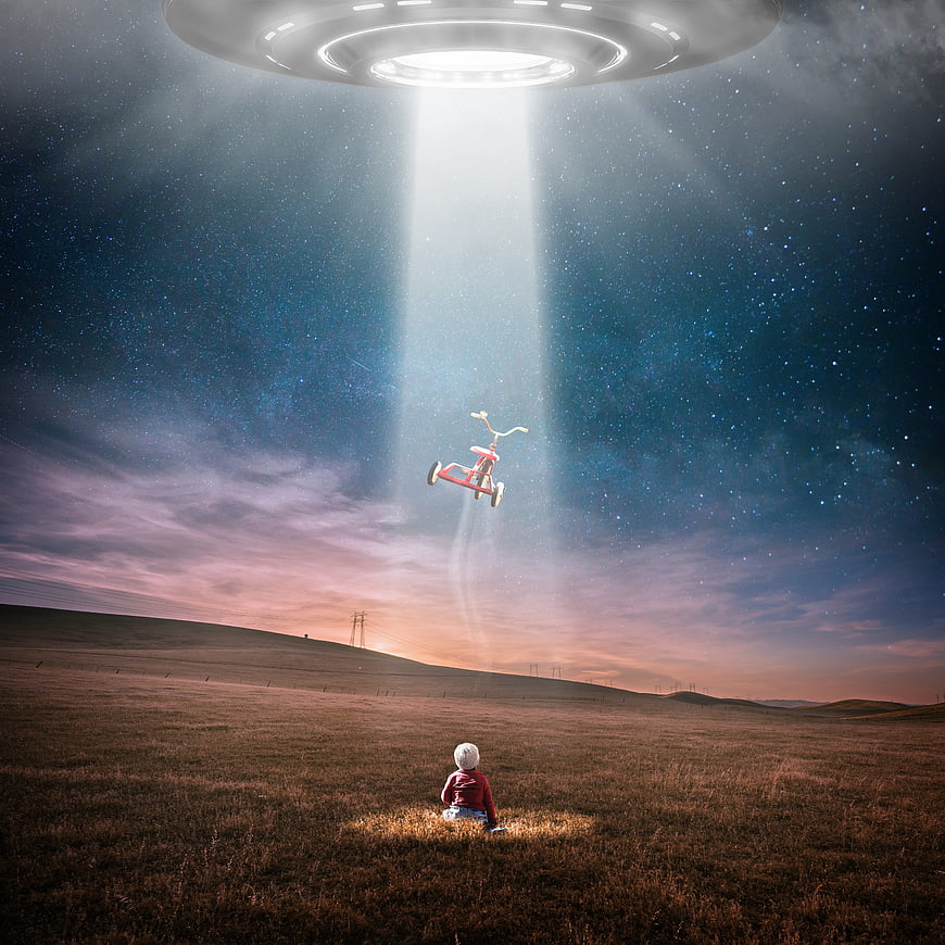 Child in field watching UFO beam lift tricycle at night