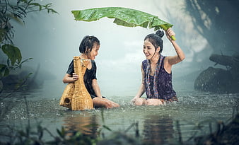 Mother and daughter playing in rain with banana leaf umbrella