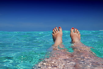 Woman's feet with red nail polish in turquoise infinity pool