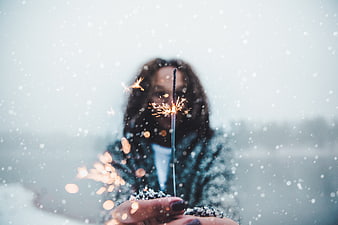 Woman holding sparkler in snow with bokeh background