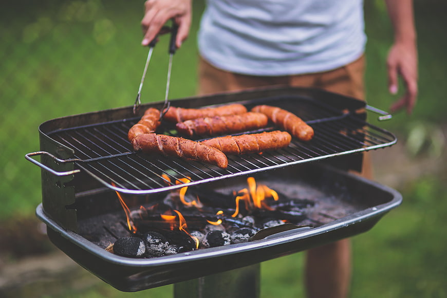 Man grilling sausages on charcoal barbecue outdoors