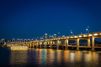 Illuminated Bridge Over River At Night With City Skyline