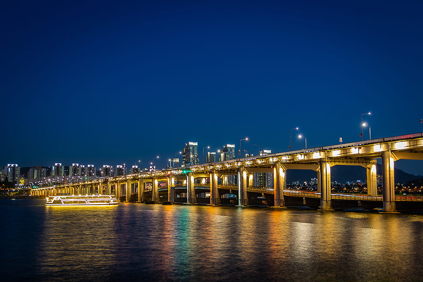 Illuminated Bridge Over River At Night With City Skyline