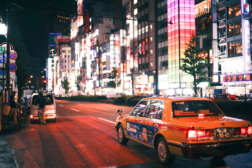 Yellow taxi driving on neon-lit Tokyo street at night
