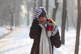 Woman in winter hat holding thermos in snowy park