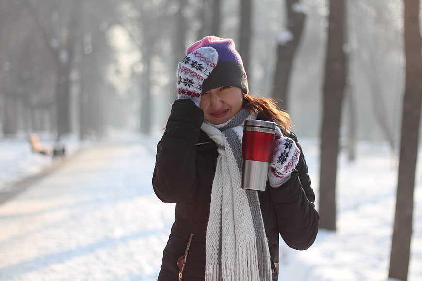 Woman in winter hat holding thermos in snowy park
