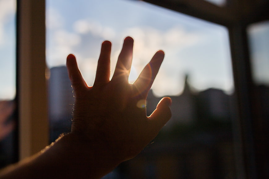 Silhouette of hand reaching for sun through window