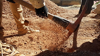 Worker Digging Red Soil with Pickaxe on Construction Site