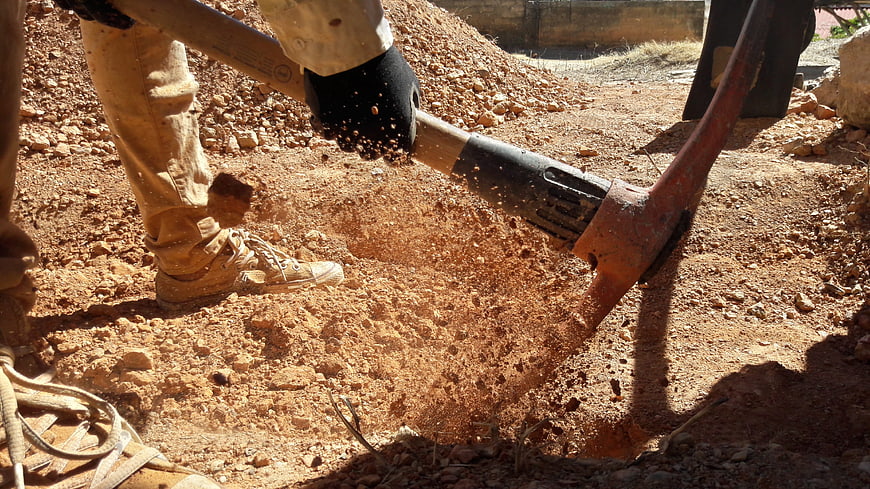 Worker Digging Red Soil with Pickaxe on Construction Site