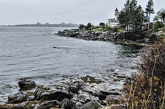 Misty coastal landscape with rocky shoreline and white house